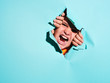 © Cien X Cien Studio/ADDICTIVE STOCK - Screaming angry boy with grimace looking through ripped blue paper sheet in studio