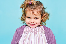 Crop Joyful Preschooler In Violet Dress And Knitted Cardigan Smiling At Camera While Standing Against Light Blue Background In Studio