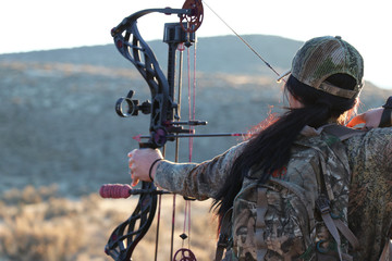 female archery hunter drawing bow
