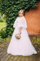 Wall Mural - Portrait of a beautiful bride in a wedding dress and a luxurious bouquet of flowers from peony roses, festive makeup and hairstyle