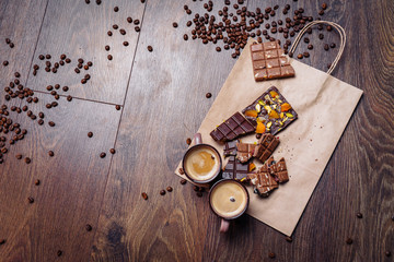 Two cups of espresso coffee with grains, craft bag and chocolate on a wooden table on a dark background. Top wiev.