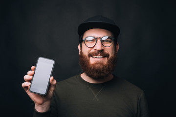 Canvas Print - Photo of Cheerful bearded man is showing blank screen phone on black background.