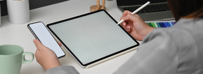 Wall Mural - cropped shot of female designer working with mock-up tablet while looking for information on smartph