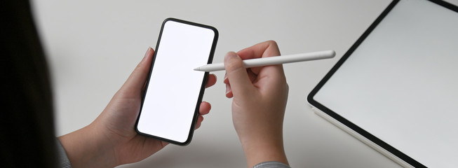 Wall Mural - close up view of female designer looking for information on horizontal mock-up smartphone