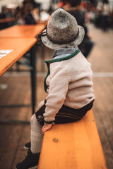 little child with traditional bavarian clothing sitting alone on a beer bench in a tent in Germany.