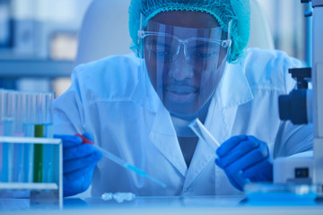 African doctor in protective mask working with samples from tube at medical laboratory