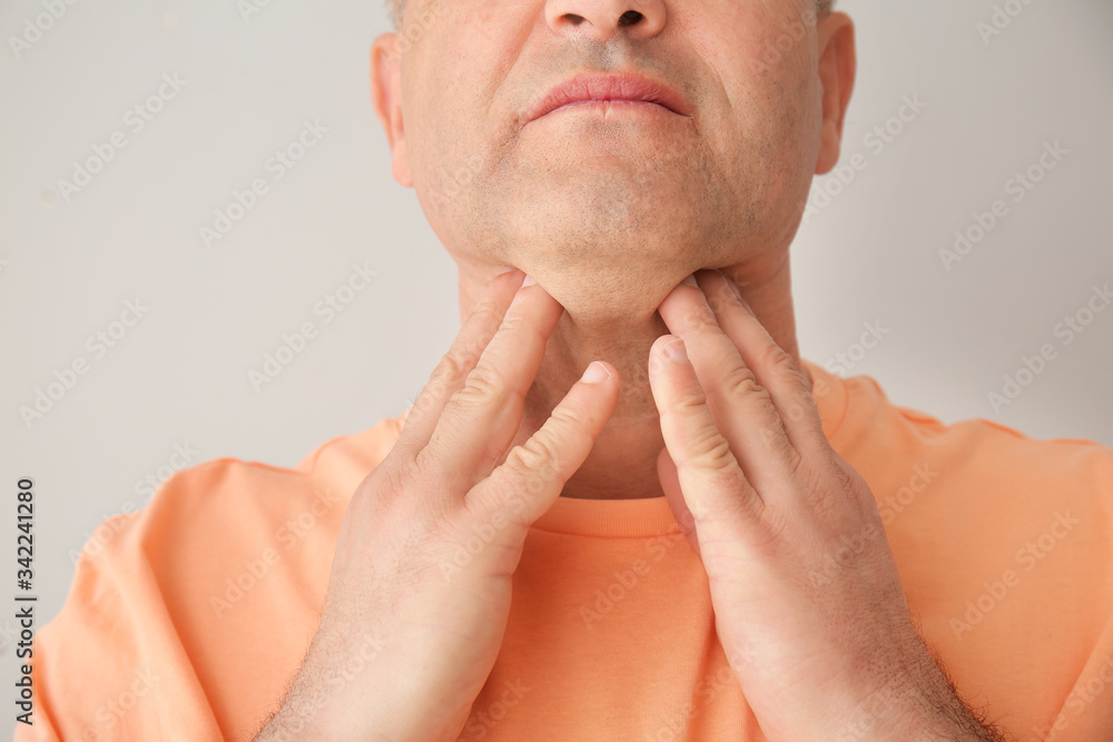 Mature man checking thyroid gland on grey background, closeup