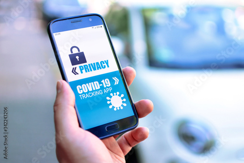 Privacy concerns with Corona Virus Tracking App concept showing hand holding cell phone with application design showing choice between app and privacy in front of blurry street background