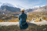 Fototapeta Krajobraz - A man with traditional dress sitting on wall and looking at Hunza valley in autumn season, Gilgit Baltistan in Pakistan