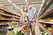 © Syda Productions - sale, family and pandemic concept - happy mother, father and daughter wearing face protective medical masks for protection from virus disease with shopping cart buying food at supermarket