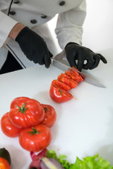 Chef cook cut tomatoes with a knife at the white table