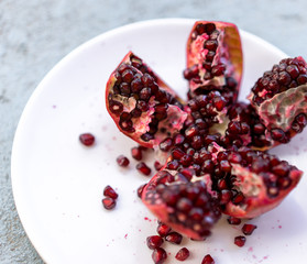 Wall Mural - A fresh red ripe juicy raw cut open pomegranate on a white plate, close up, macro view of healthy fruit, ingredient for a juice, salad, antioxidant