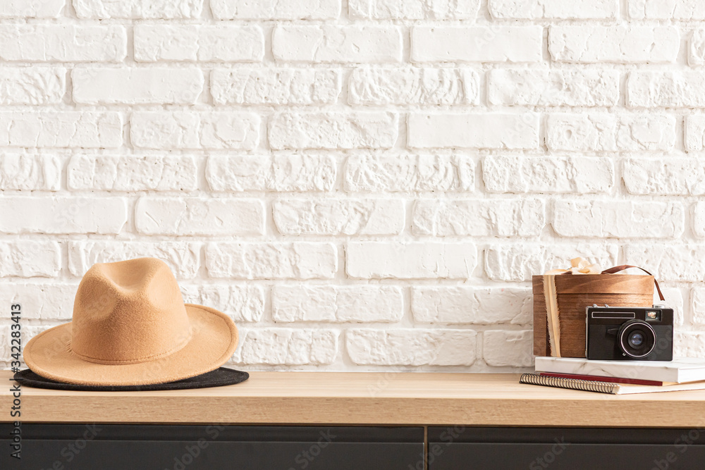 Obraz na płótnie wooden shelf with retro photo camera and hat. Stylish interior of living room with white brick wall, brown box, elegant accessories. Minimalistic concept of home decor. Template. w salonie