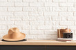 wooden shelf with retro photo camera and hat. Stylish interior of living room with white brick wall, brown box, elegant accessories. Minimalistic concept of home decor. Template.