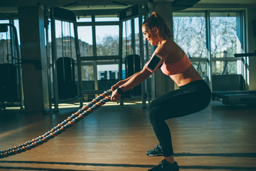 Wall Mural - Young woman with battle ropes exercise in the fitness gym