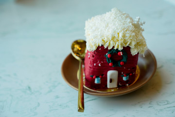 christmas red house cake decoration with golden spoon serve on table in restaurant, snow covering on roof house.