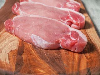 Raw uncooked fresh juicy pork chops on a wooden cutting board and simple table cloth, close up.