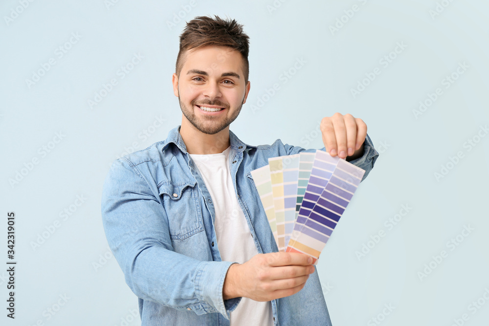 Young man with paint palette on color background