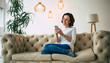 © My Ocean studio - Cozy atmosphere. Beautiful woman in casual clothes is holding a smartphone in her hands and smiles while sitting on a soft couch in a designer flat.