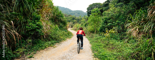 Fotomural Woman cyclist riding a bike on a nature trail in the mountains