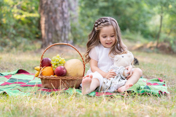 kids picnic. cute little girl embrace teddy and enjoying picnic in the park.