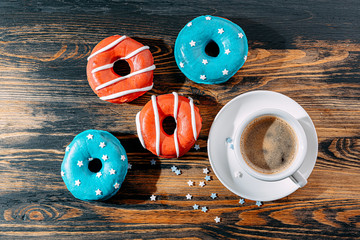 donuts one with blue icing and white stars and with red icing and white stripes and a cup of coffee on a wooden table