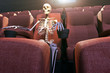 © Jose Luis Stephens - 3D rendering of a skeleton in an empty movie theatre representing bored to death and stay at home concepts