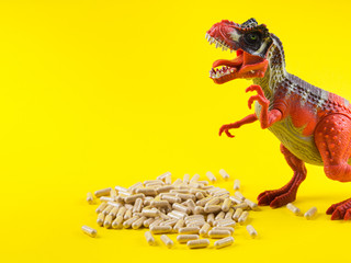 Maca powder in capsules on yellow background with funny toy dinosaur above the pills. Food supplement for energy boosting.