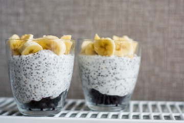 Background and two glasses with pudding chia, blackcurrant and fresh pieces of banana. Useful and delicious, with vitamins breakfast.