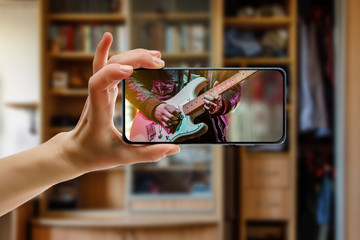 Watching online music concert at home using a mobile phone. Guitar close-up on the screen.