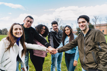 Group of young friends at the park join hands in the center of a circle to give unity and strength to everyone - Millennials in a team building moment - People have fun together