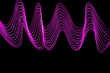 Wall Mural - Long exposure photograph of neon purple colour in an abstract swirl, parallel lines pattern against a black background. Light painting photography.