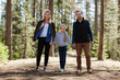 © Comeback Images - Portrait of happy family of mother, father and daughter standing in forest holding hands and looking at camera