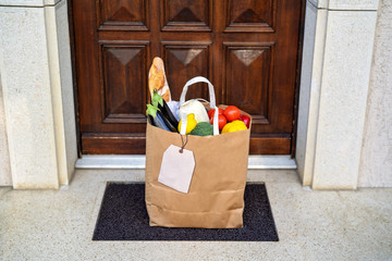 Contactless food delivery service concept. Paper bag with groceries delivered and left outside at entrance door.  Online shopping. Healthy fresh fruit and vegetables, zero waste, recyclable package.