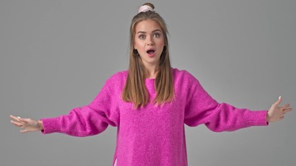 Poster - A joyful young woman is doing a magic gesture by her hands isolated over a grey background in studio