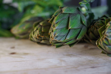 Close Up Of Thorns Leaves Of The Artichokes Freshly Picked By The Farmer Laid On A Wooden Table And Illuminated By Sunlight, Vegan And Mediterranean Cuisine Ingredients