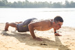 © desaart - Young athletic man doing push ups on the lake beach