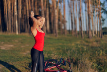 Athletic Girl Bicyclist On The Edge Of The Forest Collects Long Hair In A Ponytail. Nature, Sky, Sunset.