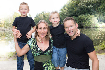 lovely parents with two little son sitting on park wooden bench in summer day aside pond lake