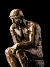A Bronze Replica Statue Of Rodin's Thinker On A Black Background