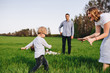 © malysheva - Family in nature. Picnic in the forest, in the meadow. Green grass. Blue clothes. Mom, dad, son with glasses. Boy with blond hair. Joy. Parents play with child. Together. Picnic basket. Food, blanket
