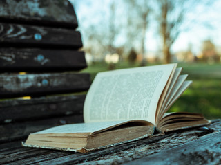 An old book lies on a wooden bench in an outdoor park at sunset