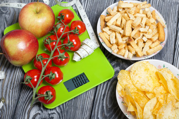 Wall Mural - Bunches of tomatoes and apples lie on the scales. Near the measuring tape. On brushed pine boards are cups with chips and crackers. Symbol of World No Diet Day.