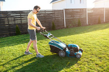 A Young Man Is Going To Mow The Lawn, He Starts A Push Lawn Mower. A Guy In Casual Yellow T-shirt And In Sunglasses