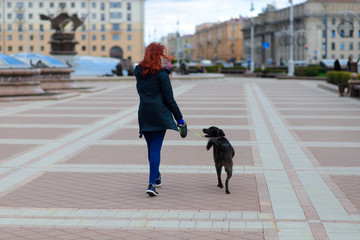 Young female using a face mask as a coronavirus spreading prevention walking with her dog. Global COVID-19 pandemic concept image.