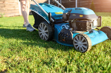 Close-up blue push lawn mower on a green grass, man on a background. A man mows grass