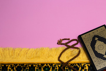 Wall Mural - Quran with skullcap and muslim rosary and prayer rug on a pink background