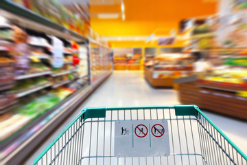 Shopping cart in supermarket with product shelves interior defocused blurred background 