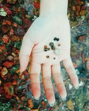 Close-up Of Woman Collecting Tiny Pebbles At Beach