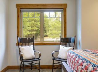 WIndow area of master bedroom with two chairs and white pillows and side of bed with quilt.